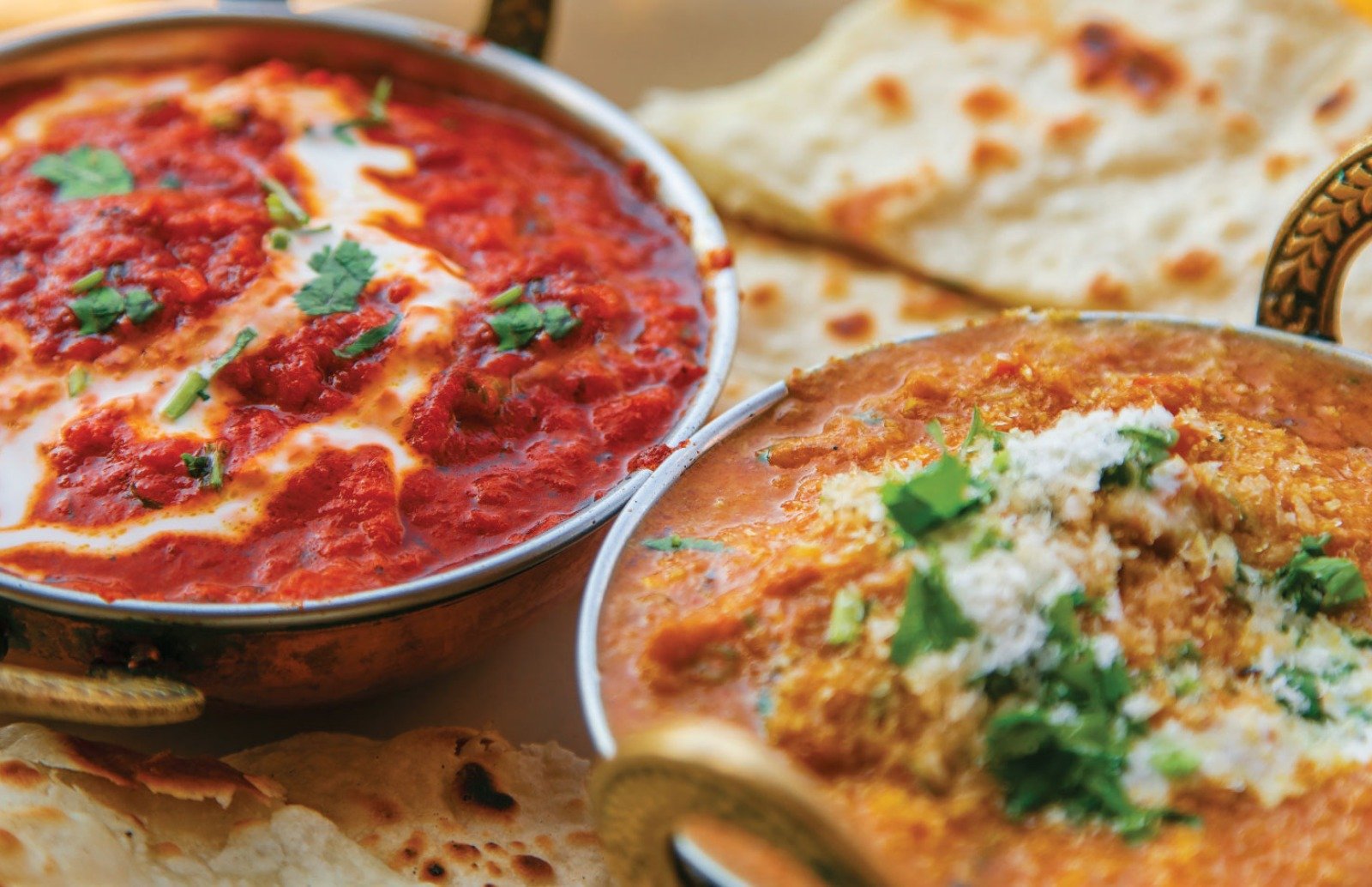 Best Curry from Amesbury Tandoori, available to takeaway Two balti bowls filled with different curries. Garnished with coriander. Naan bread resting alongside the bowls